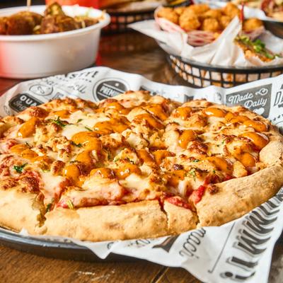 Peri Chicken Pizza with various food plates on a table, close up.
