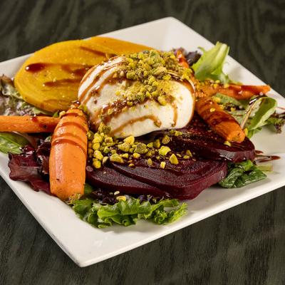 Burrata cheese topped with pistachios, with carrots, slices of red beets and yellow squash on a bed of mixed greens.