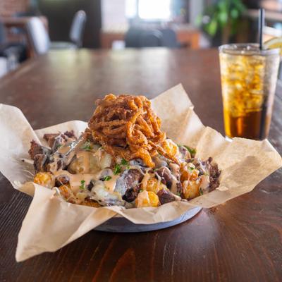 Tater tots, with brisket, sauce, cilantro, crispy onion strings and Iced Tea photo.