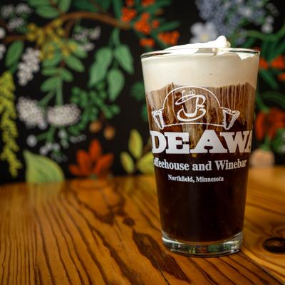 Vanilla cold brew with coconut cold foam, sits on a wooden table with a floral background.