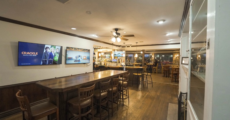 Interior, long table by a wall with two TVs, bar and seating area in the background