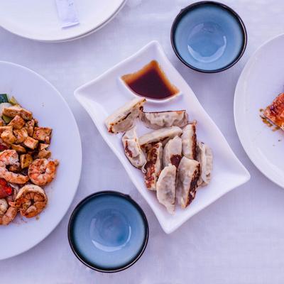 A plate of dumplings with sauce flanked by other dishes.