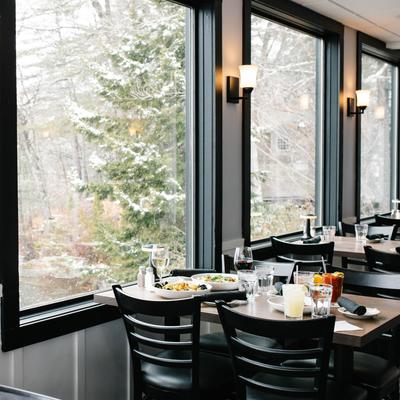 interior with large windows showing a snowy forest, a table set with food and drinks.