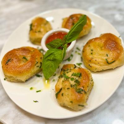 Garlic knots with a side of marinara and basil garnish.