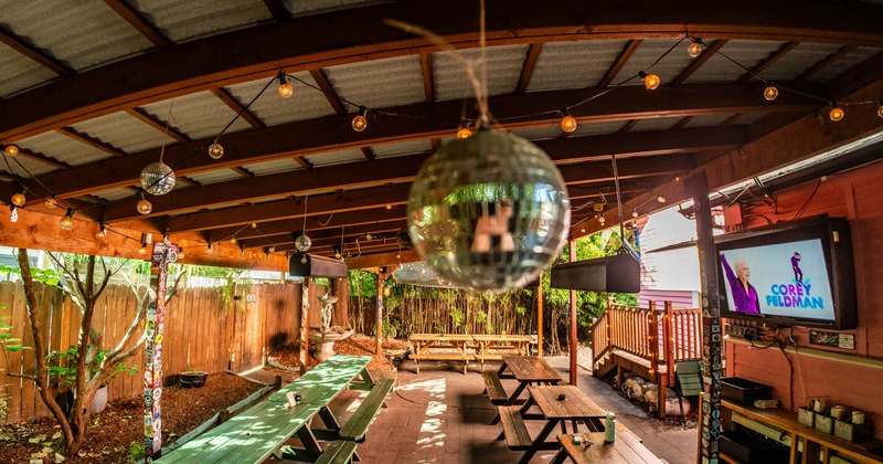 Outdoor patio area with wooden beams, string lights, picnic tables, and disco balls