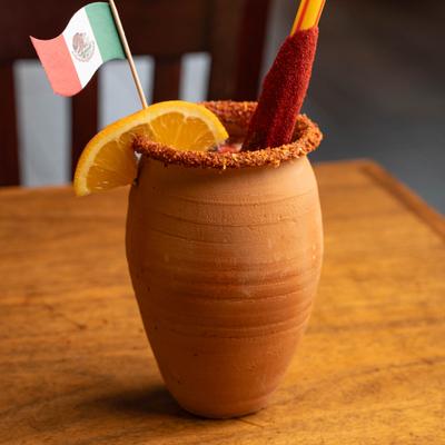 Michelada served in a clay pot with orange wedge and tamarind candy stick.