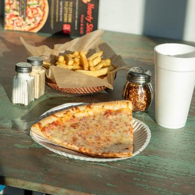 A slice of cheese pizza, fries, condiments, and a drink on the table.