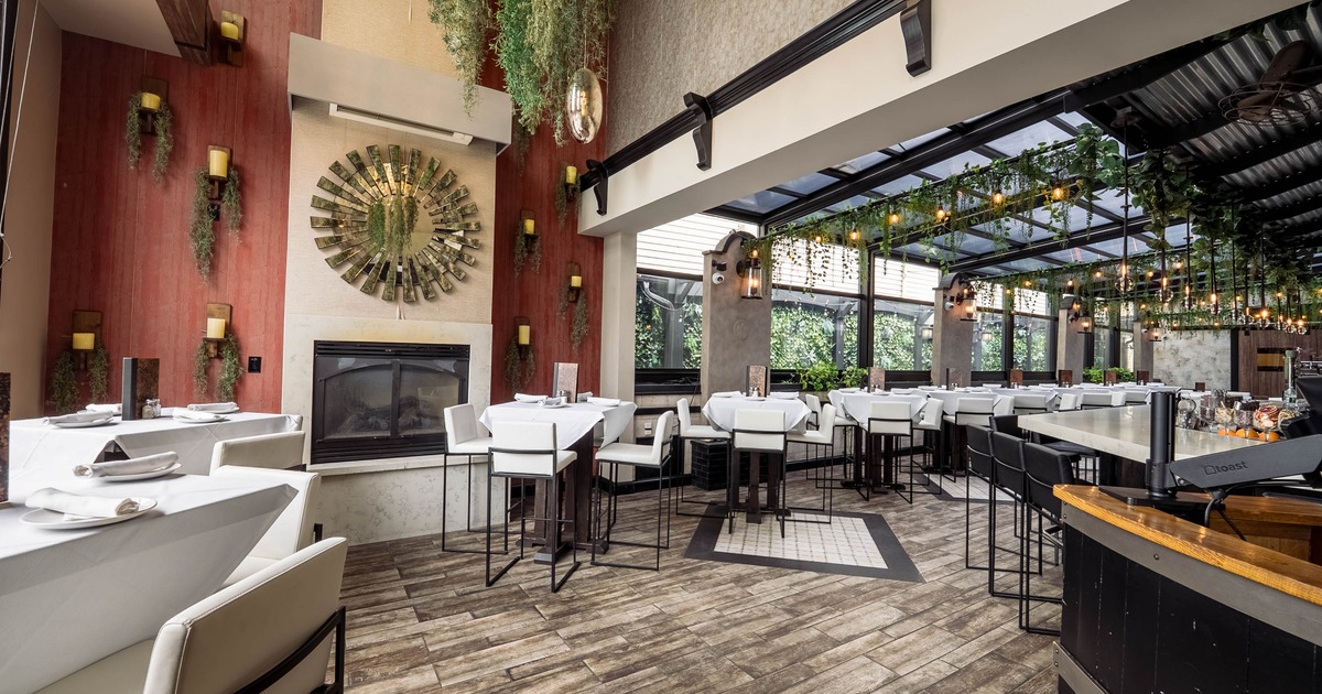 Modern restaurant interior with white tables, lush greenery and a glass ceiling