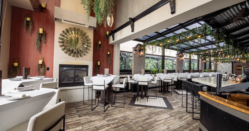 Modern restaurant interior with white tables, lush greenery and a glass ceiling