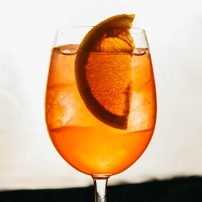 A glass of orange cocktail  glows against a soft, blurred white background.