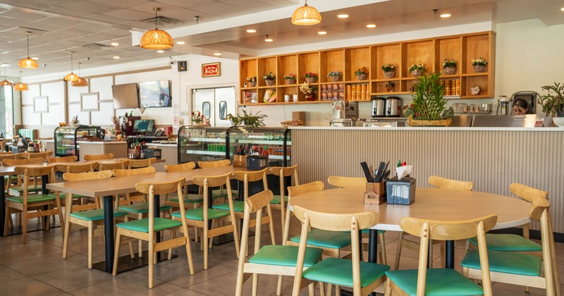 Interior - wooden tables & chairs, teal cushions, a counter displaying food items, pendant lights