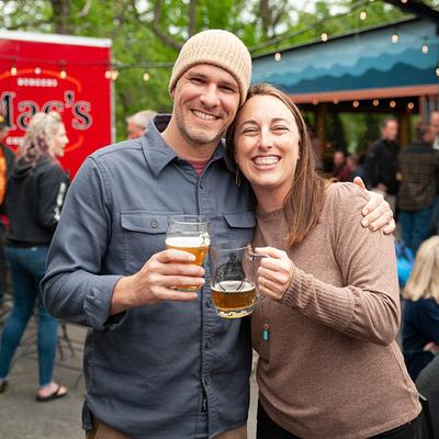 Couple smiling and holding drinks outdoors.