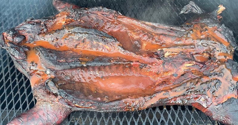 Whole smoked pig cooking on a metal barbecue grill
