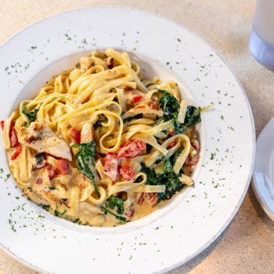 Creamy fettucine pasta with chicken, spinach, and tomatoes on a white plate.
