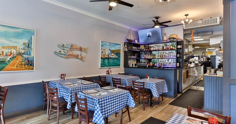 Interior with checkered tablecloths, paintings, a bar and a partially visible kitchen