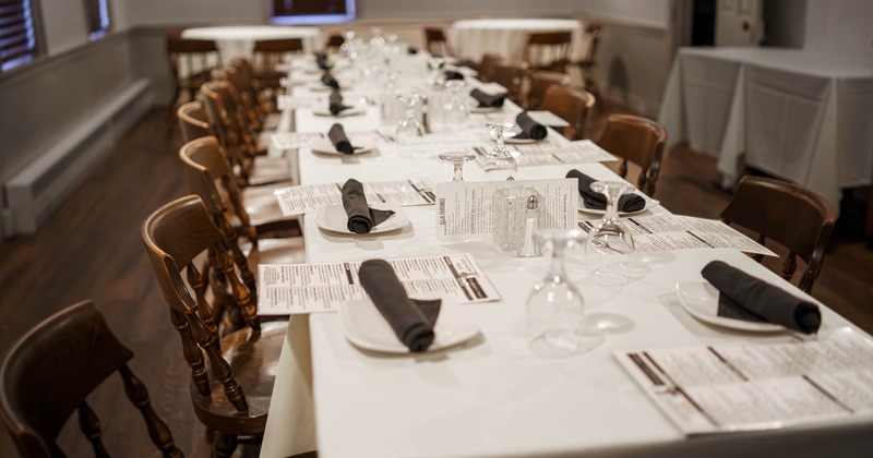 Dining area with a long table with white tablecloths, black napkins and clear wine glasses