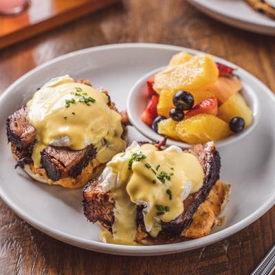 Brisket eggs Benedict with hollandaise sauce, chives, and a fruit salad