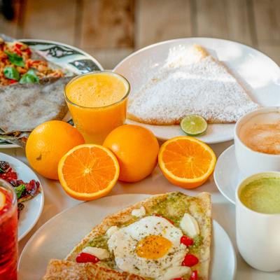 Breakfast with egg and pesto crepe, powdered sugar crepe, fresh oranges, juice, and lattes.
