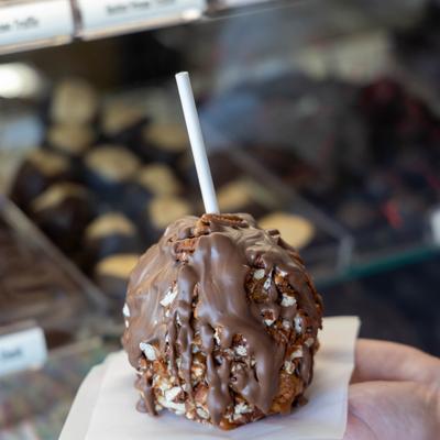 A hand holds a gourmet caramel apple coated in pecans and drizzled with chocolate.
