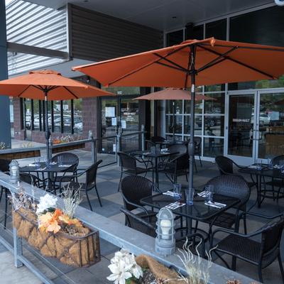 Outdoor patio of a restaurant with black wicker chairs, tables, and orange umbrellas.