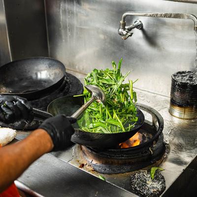Fresh greens being stir-fried in a hot wok over an open flame.