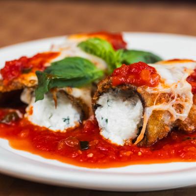 Eggplant rollatini in marinara topped with basil leaves.