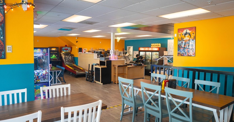 Interior - bright orange and teal walls, white tables and chairs and arcade games in the background.