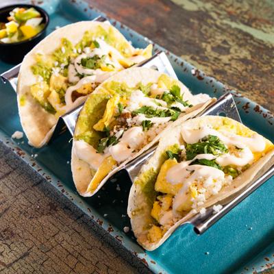 Three tacos with green sauce, cilantro, and crema.