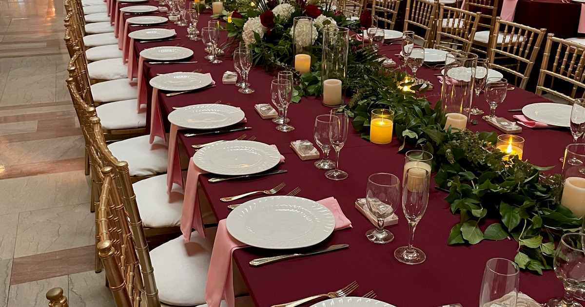 Banquet table setup with a burgundy tablecloth, napkins, plates and glasses