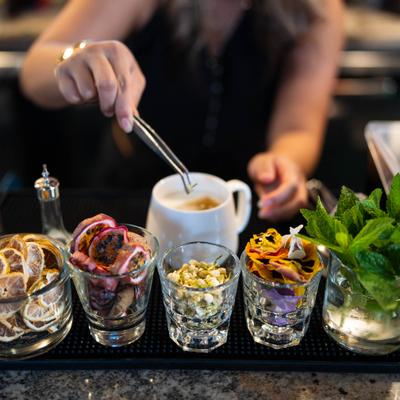 Bartender in action behind several small glass containers with cocktail garnishes.