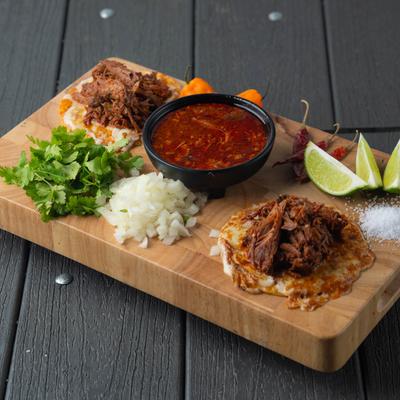 Quesabirria tacos with goat meat, served with cilantro, onion, peppers, and birria sauce.
