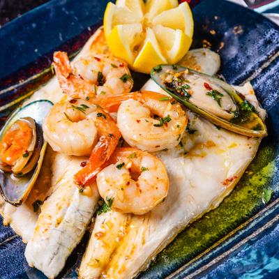 Fish fillets topped with sautéed shrimp and mussels, garnished with lemon.