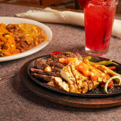 A sizzling fajita platter with sides of rice and refried beans, accompanied with a margarita.