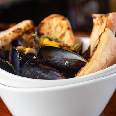 Mussels Provencal served in a white bowl with grilled crostini.