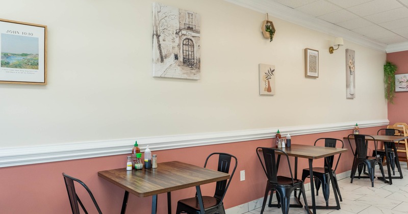 Interior - wooden tables, black metal chairs, framed artwork on cream and pink walls,