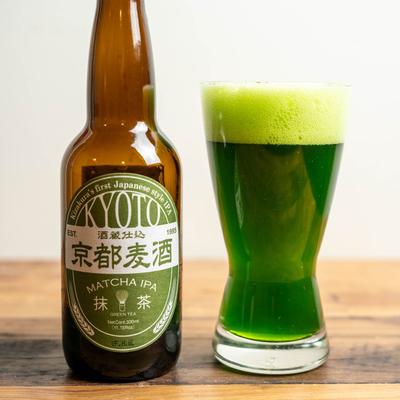 A bottle of Kyoto Matcha IPA stands beside a glass with the green beer on a wooden surface.