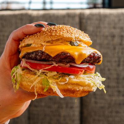 Hand holding a cheeseburger with lettuce, onion and tomato.