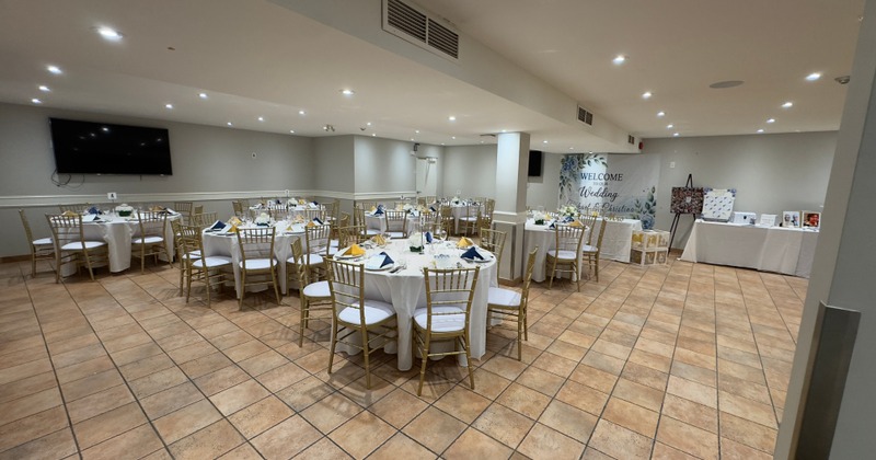 Indoor banquet hall set up for a celebration with round tables and white tablecloths