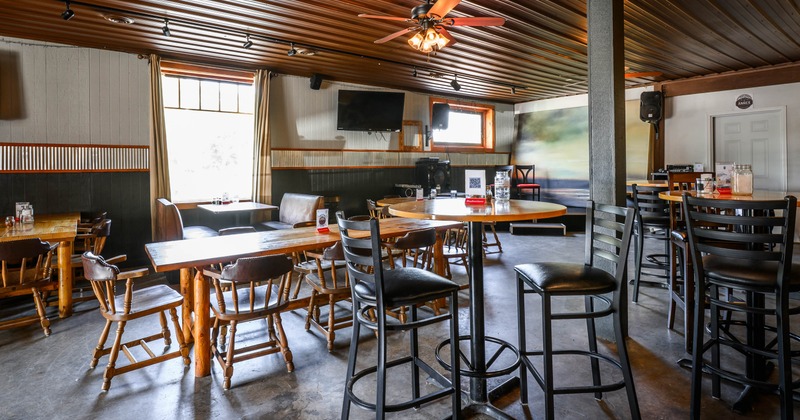 A casual interior - wooden tables and chairs, a leather booth, large windows, ceiling fans.