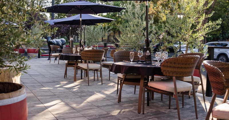 Outdoor patio - umbrellas, set tables, woven chairs, potted olive trees & a black bull statue
