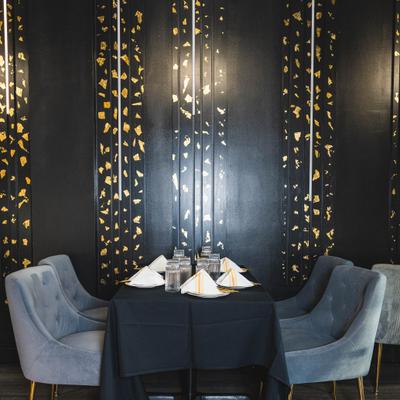 A restaurant table for four, gray chairs and a black tablecloth against a black-gold-patterned wall.