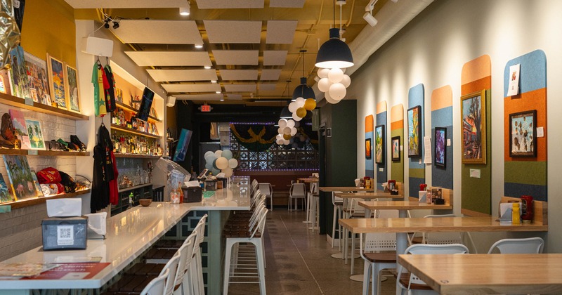 Interior of a restaurant with a bar on the left and tables on the right, decorated with artwork