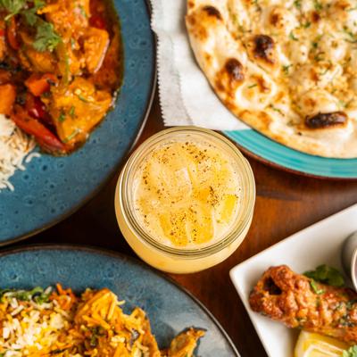 Mango Lassi glass surrounded by various food dishes, top down view.