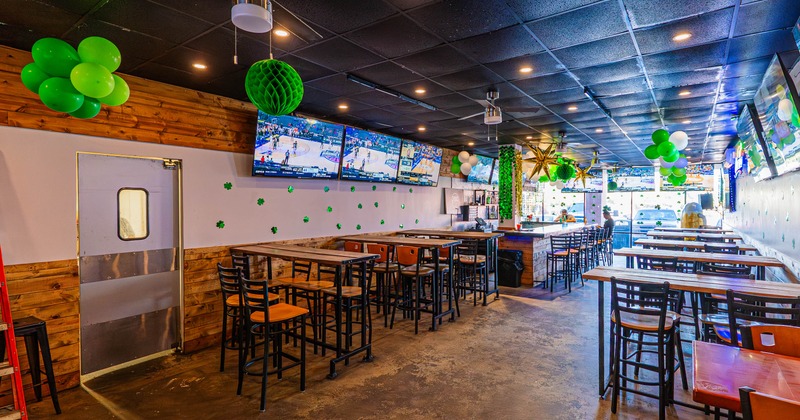 Bar interior with festive green decorations and flat-screen TVs showing a sports game