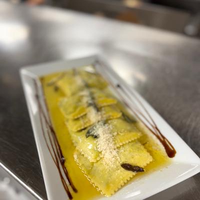 Ravioli served in a glossy yellow butter sauce, garnished with herbs and grated cheese.