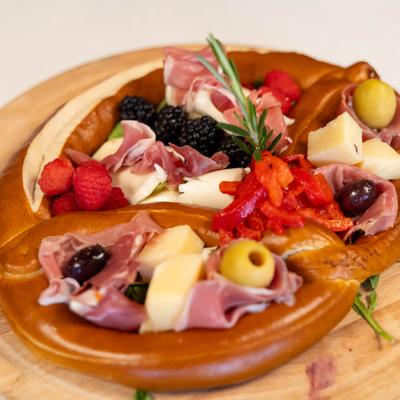 Charcuterie Board featuring a pretzel loaded with specialty meats, cheeses and berries.