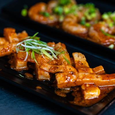 Marinated cuts of meat served on a dark plate and garnished with sliced spring onions.