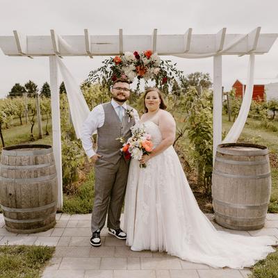 Wedding couple standing underneath the arch between two barrels at the vineyard ceremony at Next Chapter Winery.