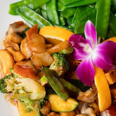 Stir-fried chicken with vegetables, orange slices, and orchid garnish.