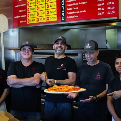 Kitchen staff posing in uniforms, one of them holding a pizza on a peel.